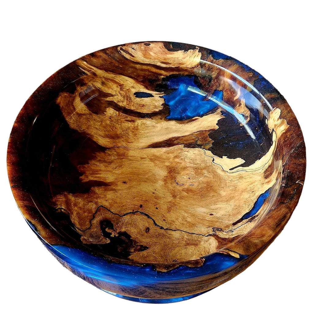 A handmade resin bowl with a swirling pattern of natural wood grain and bright blue resin, displayed on a rustic wooden surface.